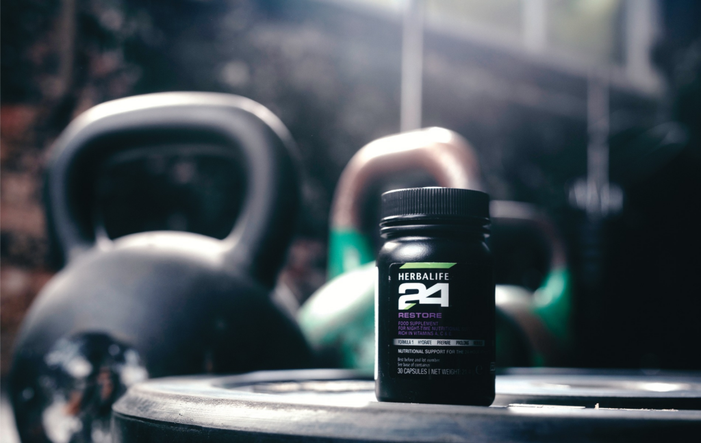 Dose Herbalife24 Restore Nahrungsergänzungsmittel für die Nacht mit Informed-Sport Logo auf einem Holztisch neben einem Wasserglas.