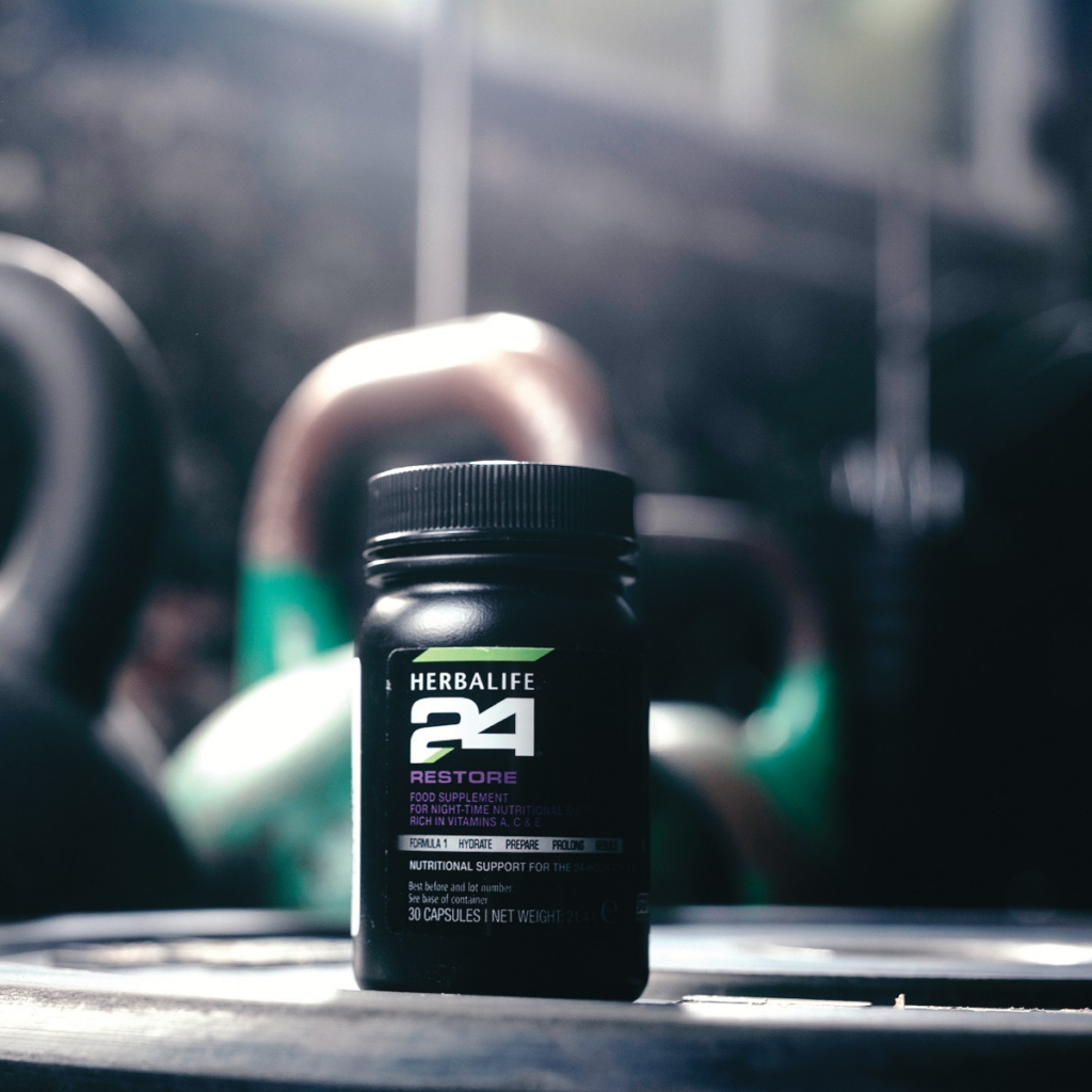 Dose Herbalife24 Restore Nahrungsergänzungsmittel für die Nacht mit Informed-Sport Logo auf einem Holztisch neben einem Wasserglas.