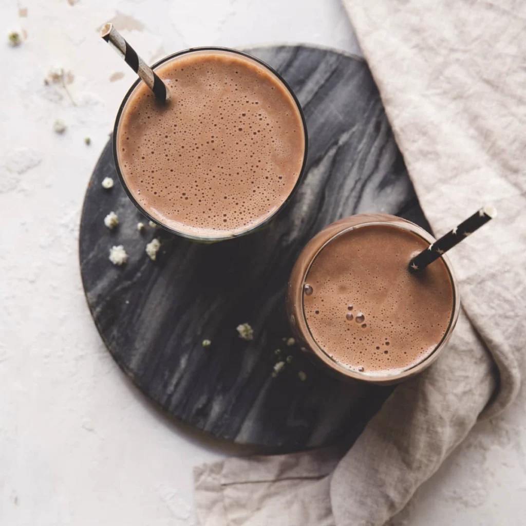 Herbalife Formula 1 Shake Smooth Chocolate zubereitet in zwei Gläsern auf einem dunklen Marmorteller aus der Vogelperspektive