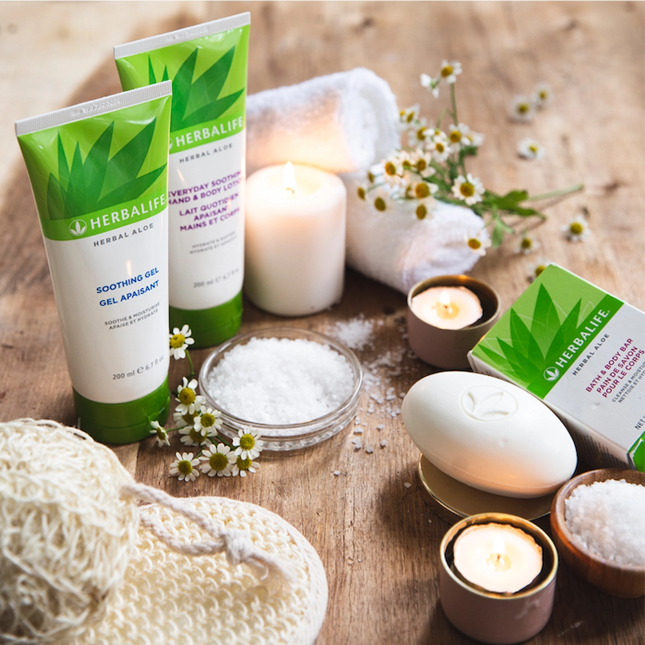 Herbalife Herbal Aloe Pflegeprodukte wie Soothing Gel und Lotion auf einem Holztisch mit Kerzen, Kamille und Badesalz für Spa.
